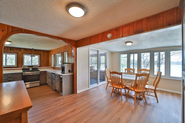 dining area featuring a textured ceiling, arched walkways, plenty of natural light, light wood-type flooring, and wood walls