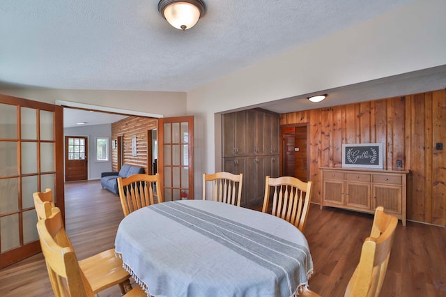 dining room featuring a textured ceiling, french doors, dark wood finished floors, and wood walls