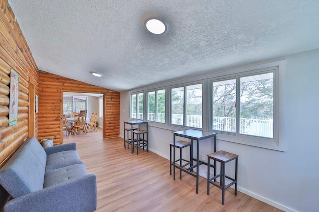 living area with a textured ceiling, log walls, wood finished floors, baseboards, and lofted ceiling