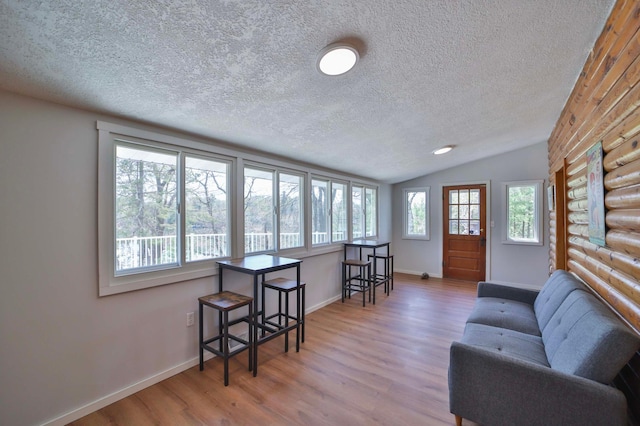 living room featuring a textured ceiling, wood finished floors, vaulted ceiling, baseboards, and rustic walls