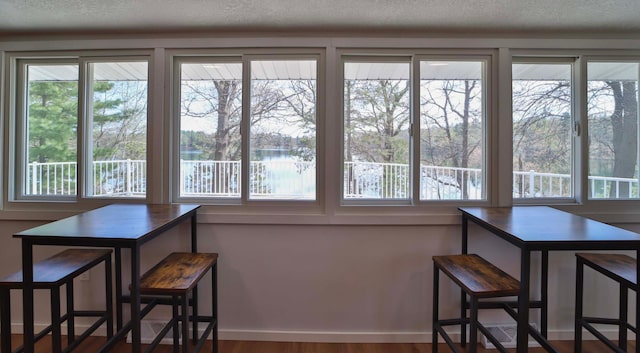 dining space with a water view, plenty of natural light, a textured ceiling, and wood finished floors