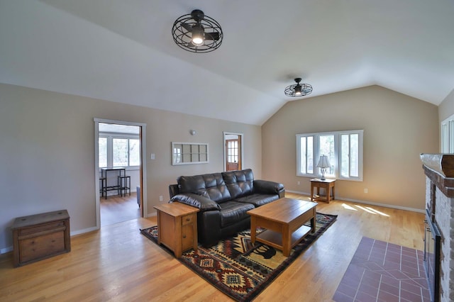 living room featuring plenty of natural light, light wood-style floors, a brick fireplace, lofted ceiling, and baseboards