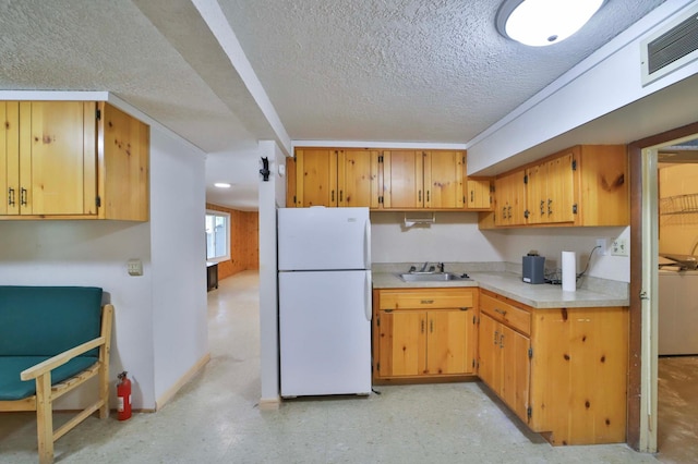 kitchen featuring freestanding refrigerator, a sink, a textured ceiling, light countertops, and light floors