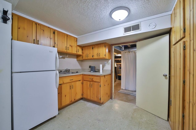 kitchen with freestanding refrigerator, a textured ceiling, a sink, and light countertops