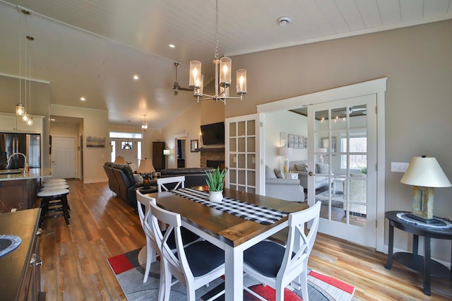 dining area with an inviting chandelier, a fireplace, vaulted ceiling, and wood finished floors