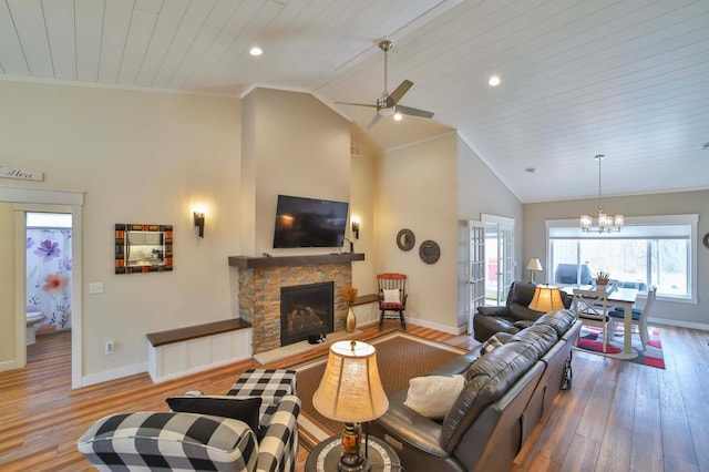 living room featuring a stone fireplace, wood finished floors, baseboards, ceiling fan with notable chandelier, and recessed lighting