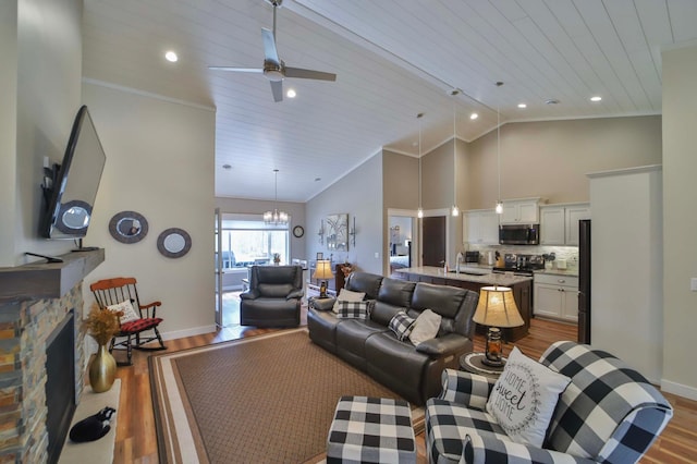living room with dark wood-style flooring, a stone fireplace, baseboards, high vaulted ceiling, and ceiling fan with notable chandelier