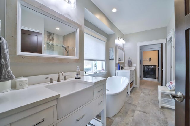 bathroom featuring a freestanding tub, a tile shower, two vanities, a sink, and washer / dryer