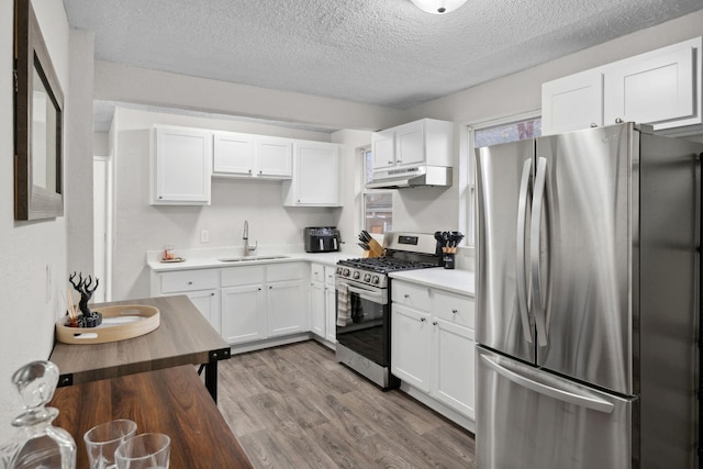 kitchen featuring a textured ceiling, a sink, under cabinet range hood, stainless steel appliances, and white cabinetry