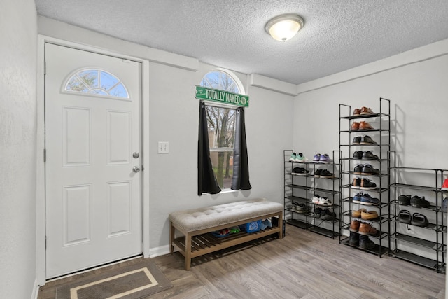 foyer entrance with baseboards, a textured ceiling, and wood finished floors