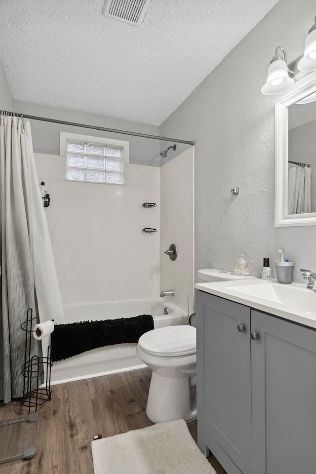 bathroom featuring vanity, a textured ceiling, shower / bathtub combination with curtain, wood finished floors, and visible vents