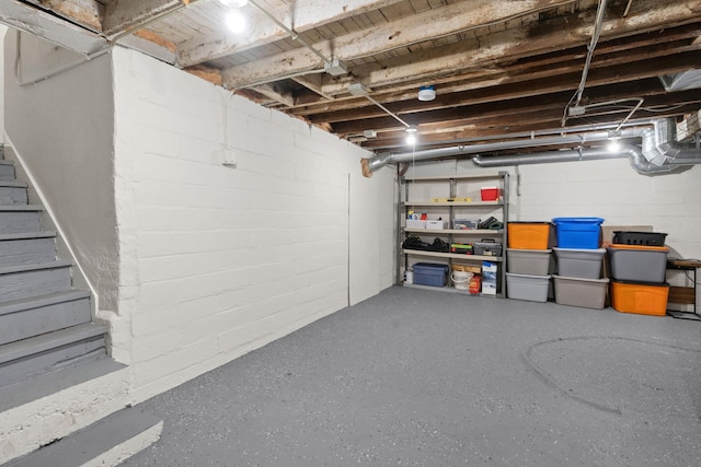 unfinished basement featuring stairway and concrete block wall