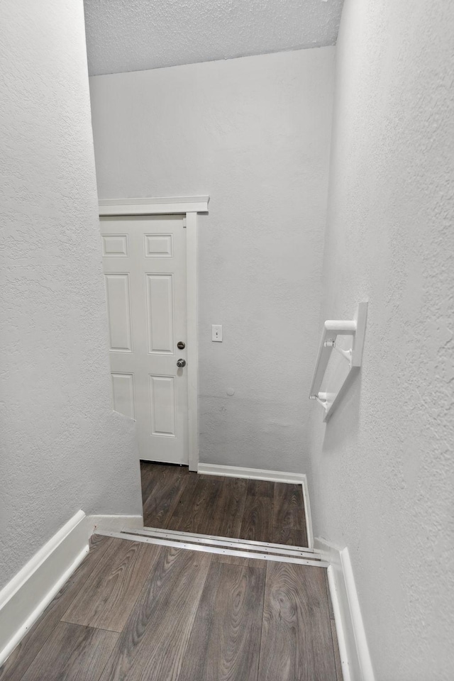 stairway featuring baseboards, a textured wall, and wood finished floors