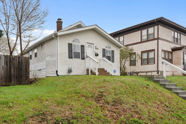 view of front facade with entry steps, fence, a chimney, and a front lawn