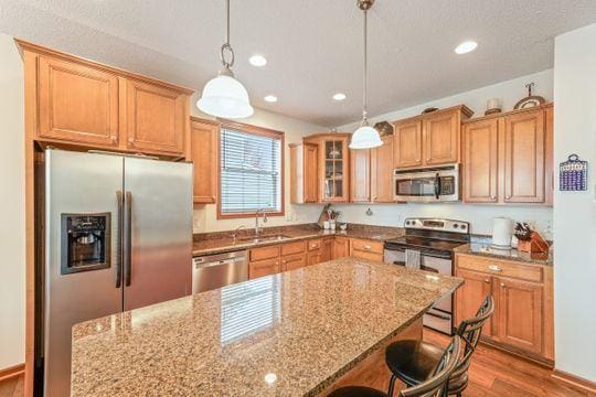 kitchen featuring stainless steel appliances, a sink, a kitchen breakfast bar, recessed lighting, and light stone counters