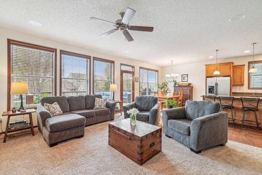 living room featuring a textured ceiling, light colored carpet, ceiling fan, a chandelier, and recessed lighting