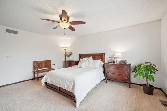 bedroom with light colored carpet, baseboards, a ceiling fan, and a textured ceiling