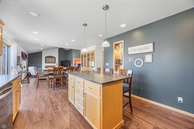kitchen with a kitchen breakfast bar, light brown cabinetry, dark countertops, stainless steel dishwasher, and wood finished floors