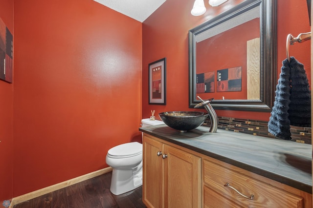 half bath featuring vanity, baseboards, wood finished floors, and toilet