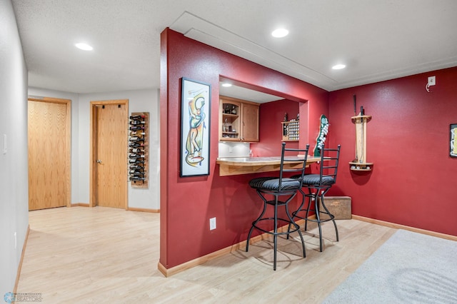 bar featuring light wood-type flooring, recessed lighting, baseboards, and indoor bar