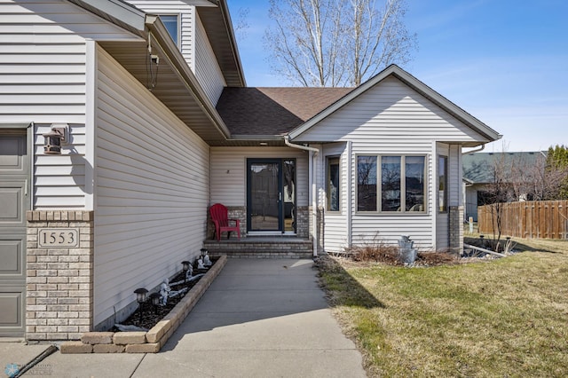 doorway to property featuring fence, a yard, and roof with shingles