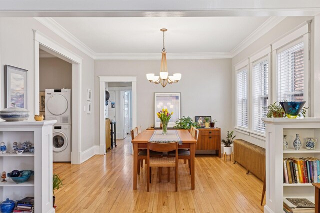 dining space featuring light wood-type flooring, stacked washer and dryer, crown molding, and an inviting chandelier
