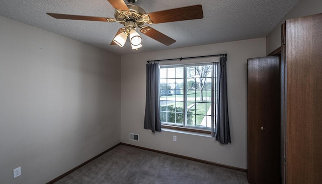 empty room featuring healthy amount of natural light, carpet floors, ceiling fan, baseboards, and a textured ceiling