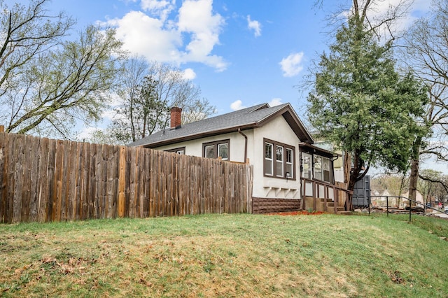 view of side of home with a yard, fence, a chimney, and stucco siding