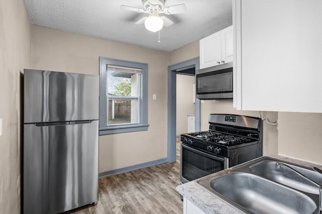 kitchen with light wood-type flooring, a textured ceiling, white cabinets, a sink, and stainless steel appliances