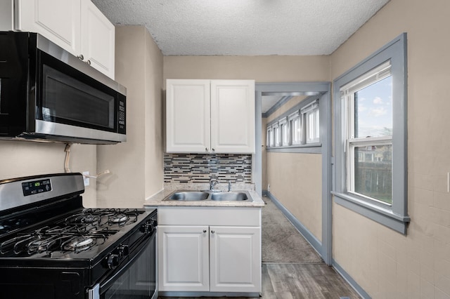 kitchen featuring white cabinets, a sink, gas range, stainless steel microwave, and light wood-type flooring