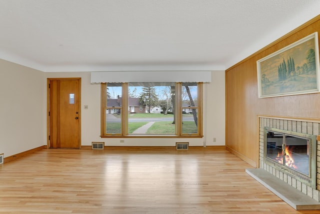 unfurnished living room featuring baseboards, a brick fireplace, light wood finished floors, and visible vents