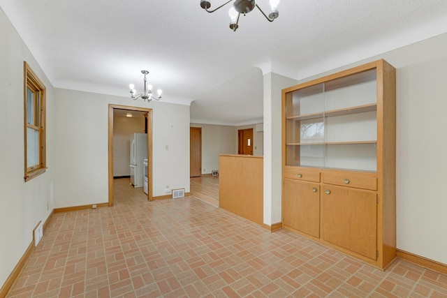 spare room with baseboards, a notable chandelier, brick patterned floor, and visible vents