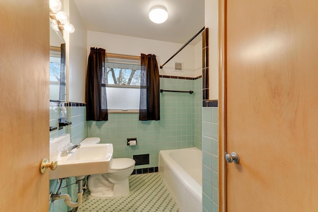 bathroom featuring shower / bathtub combination, toilet, tile walls, and wainscoting