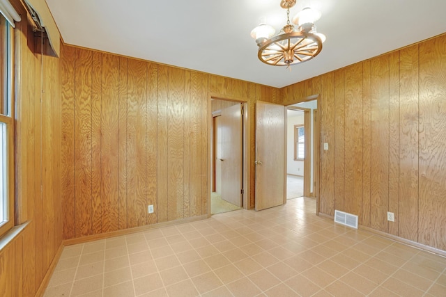 empty room with an inviting chandelier, wooden walls, and visible vents