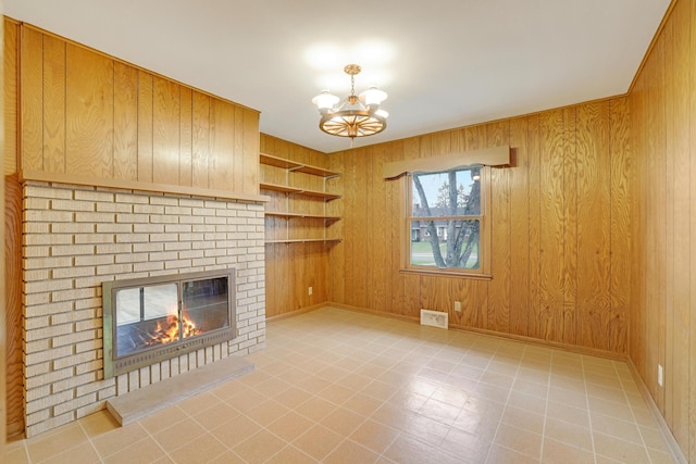 unfurnished living room featuring wooden walls, a fireplace, a chandelier, and visible vents