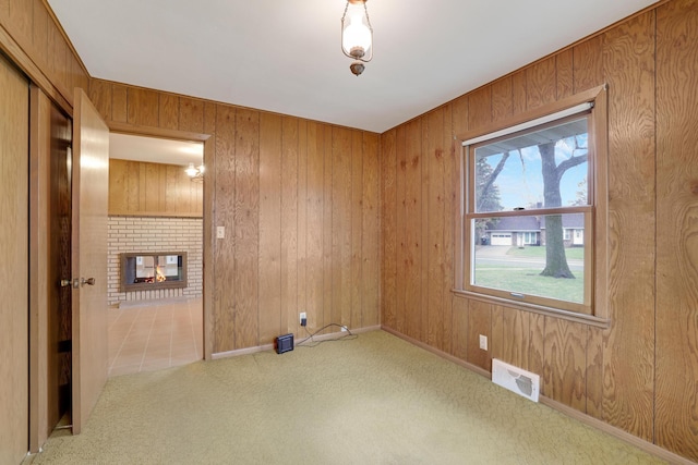 carpeted spare room featuring a brick fireplace, wood walls, and visible vents