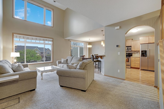 living room with arched walkways, baseboards, light carpet, and a towering ceiling