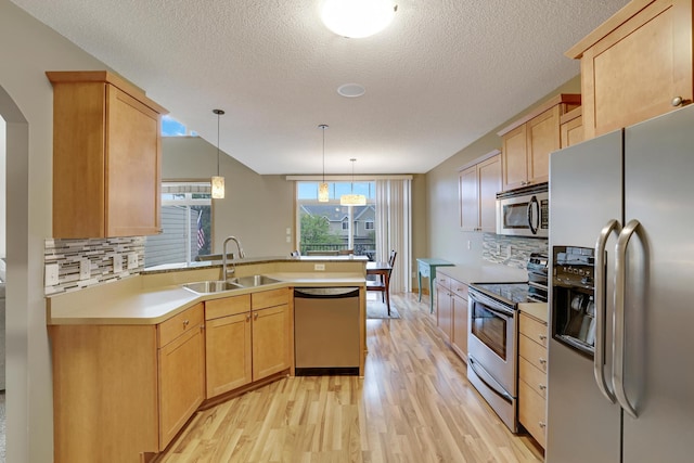 kitchen featuring decorative backsplash, a sink, a peninsula, light wood-style floors, and stainless steel appliances