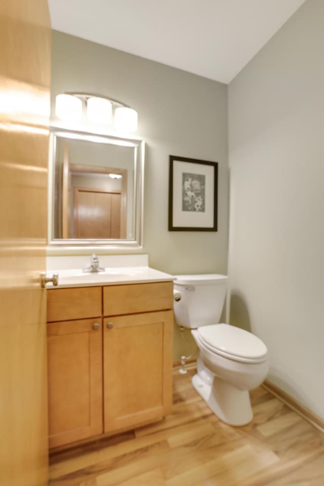 half bath featuring toilet, baseboards, wood finished floors, and vanity
