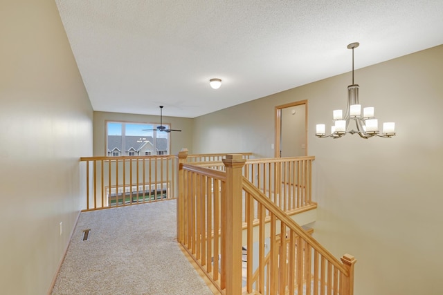 hallway featuring visible vents, an upstairs landing, baseboards, a chandelier, and carpet flooring
