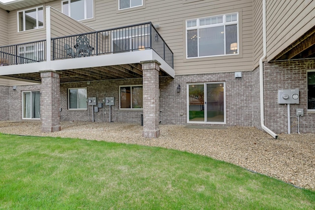 rear view of property featuring a yard, brick siding, and a balcony