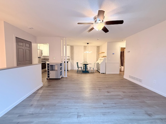unfurnished living room with visible vents, baseboards, wood finished floors, and ceiling fan with notable chandelier