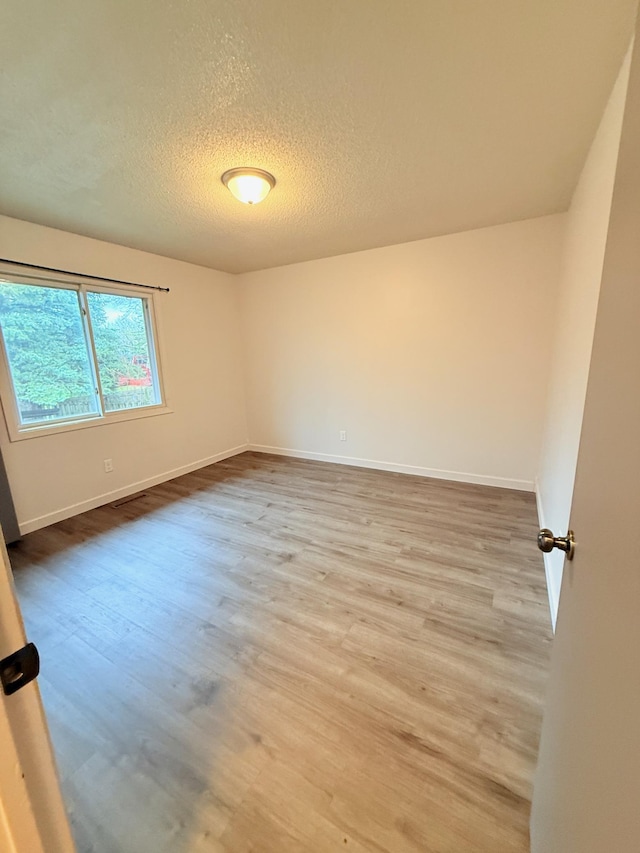 empty room with baseboards, wood finished floors, and a textured ceiling