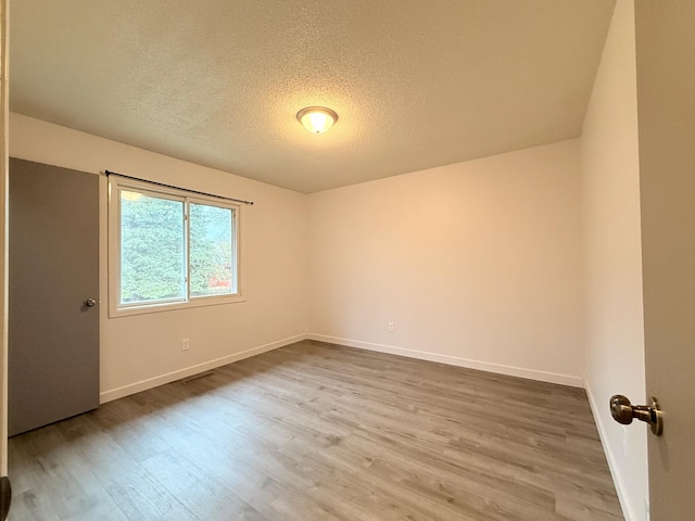 empty room featuring a textured ceiling, visible vents, wood finished floors, and baseboards