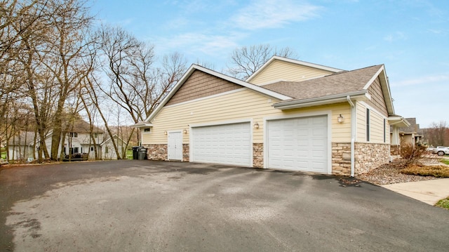 3219 Anric Dr, Eau Claire, WI 54701 - view of property exterior featuring a garage, a shingled roof, stone siding, and aphalt driveway