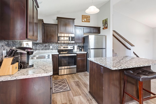 kitchen with appliances with stainless steel finishes, tasteful backsplash, vaulted ceiling, dark brown cabinets, and light wood finished floors