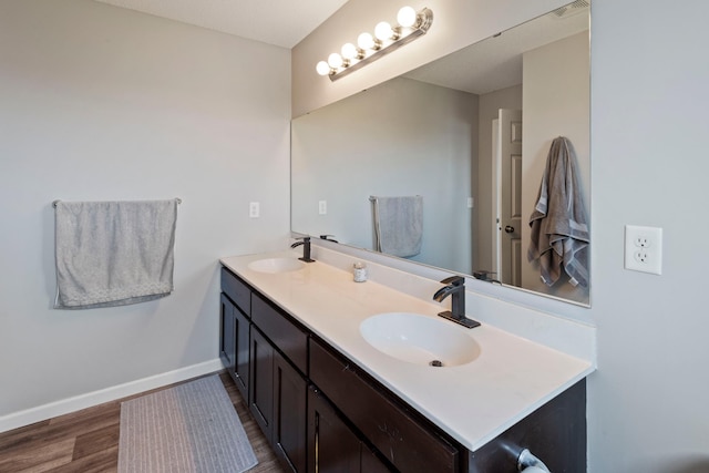 bathroom featuring a sink, baseboards, double vanity, and wood finished floors