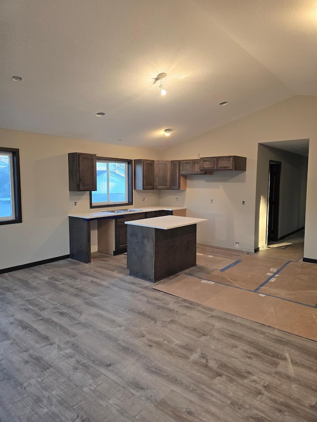 kitchen with light countertops, dark brown cabinetry, a kitchen island, and lofted ceiling