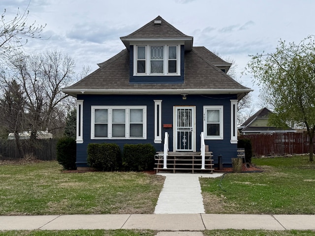 bungalow-style home featuring fence, a shingled roof, and a front yard