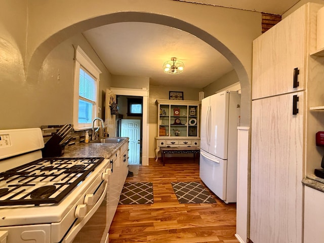 kitchen featuring a sink, arched walkways, white appliances, and wood finished floors